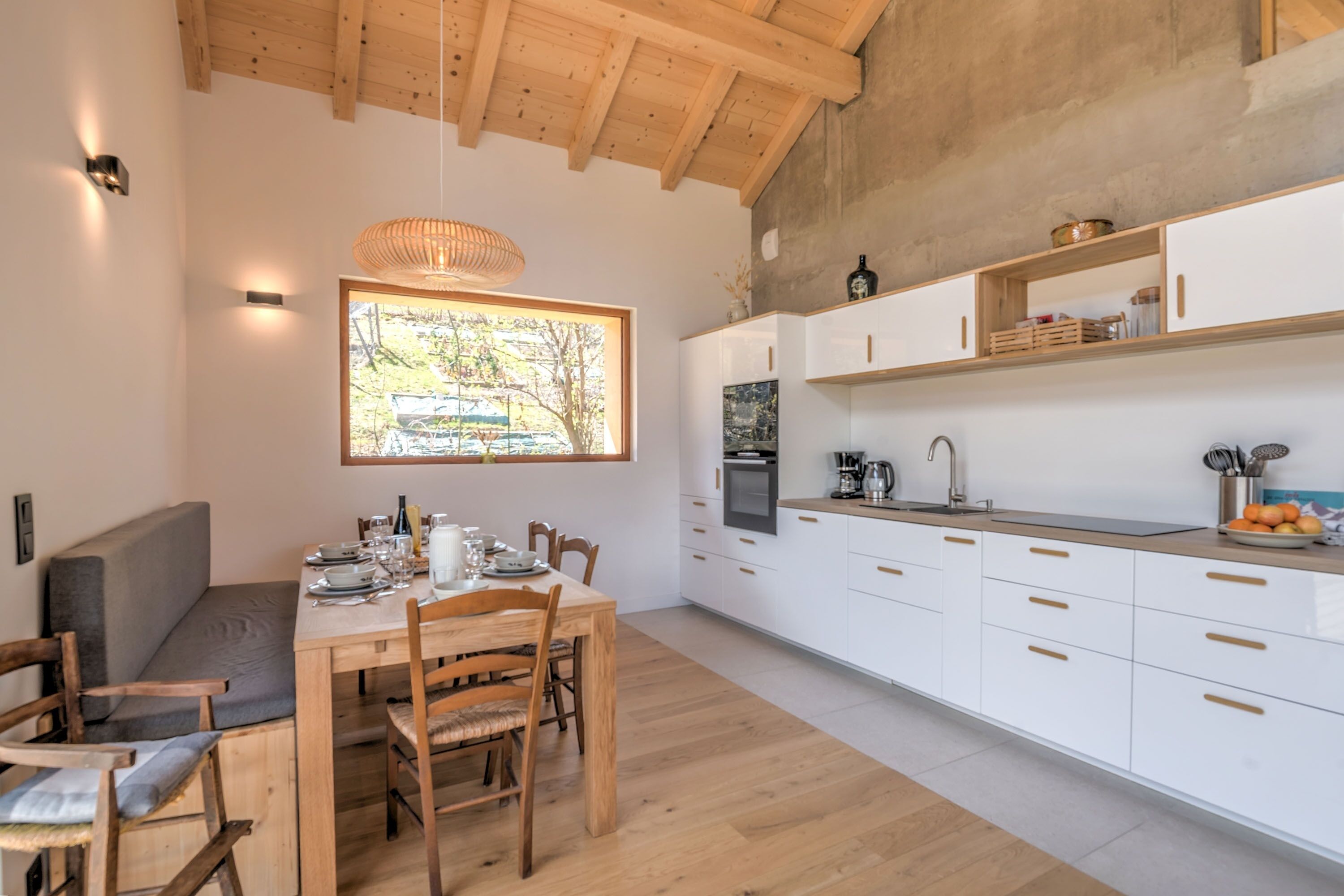 A modern kitchen with white cabinets, a wooden dining table, and a large window.