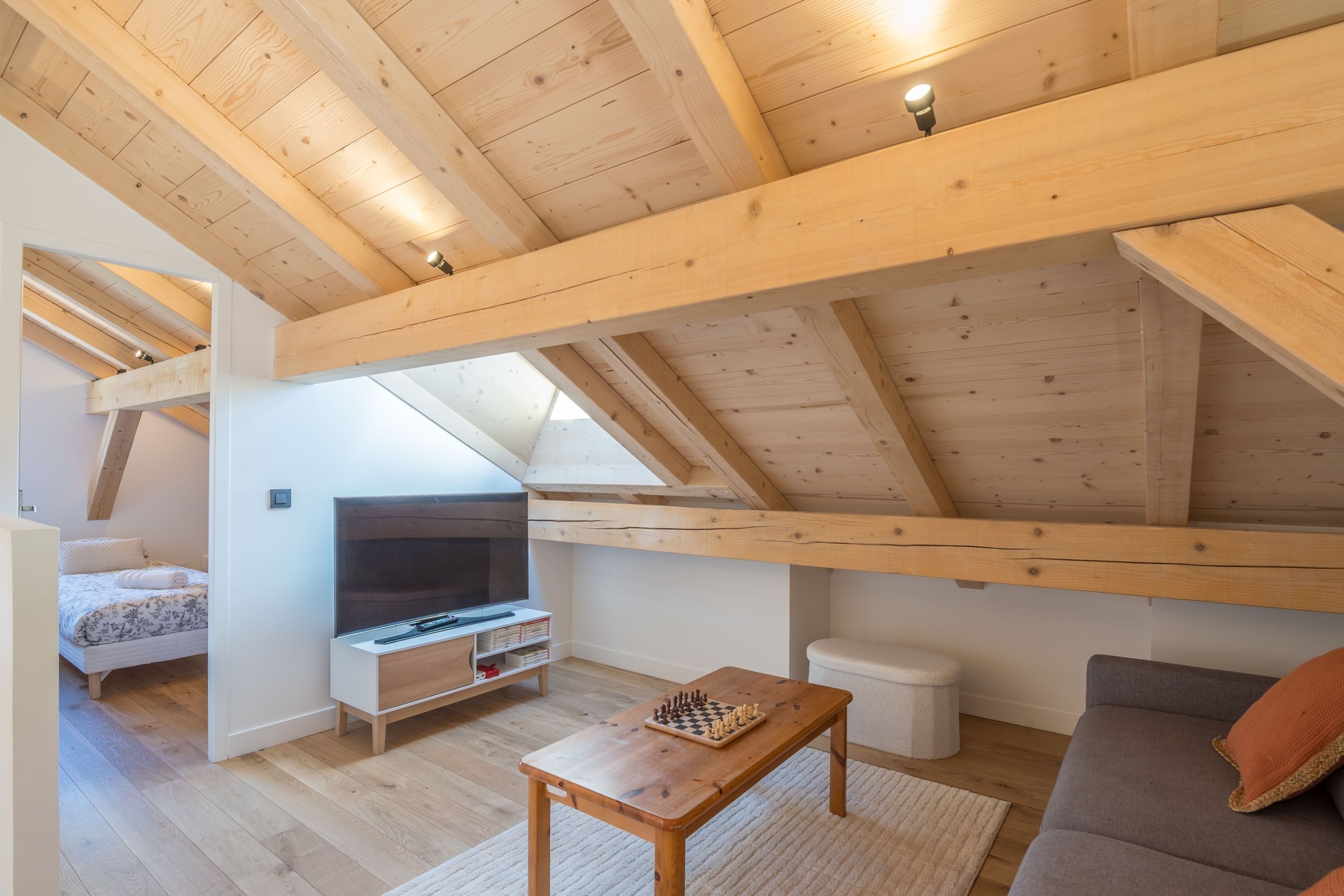 Un habitación estilo loft con techo de madera, televisor, un tablero de ajedrez, un sofá y una pequeña mesa.