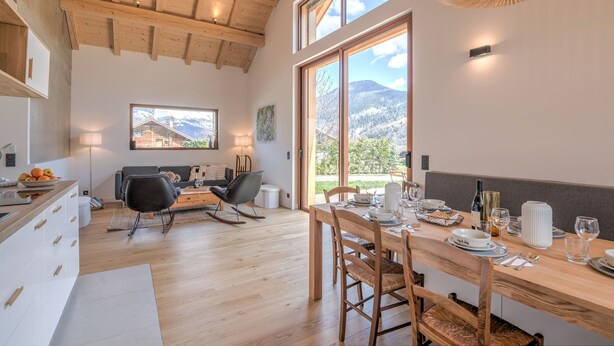 A modern kitchen with wooden beams, a dining area with a table set for two, and a large window with a mountain view. - Le Chalet Morets - Avec vue sur la montagne (Saint-Gervais-les-Bains)