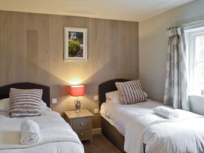 Ein Doppelzimmer mit zwei Betten, einem Nachttisch mit Lampe, einem gerahmten Bild an der Wand und einem Fenster mit Vorhängen.
