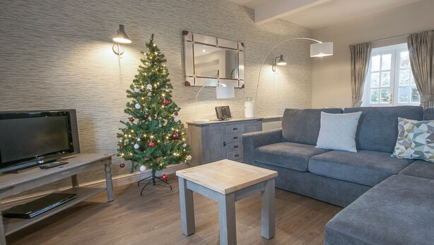 Ett modernt vardagsrum med en tv, en julgran, en soffa och ett soffbord.