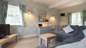 A living room with a sofa, a TV, a small table, and a mirror. - Spacious stone cottage set in beautiful woodland with lovely views over a lake. (Darwin Lake, near Matlock)