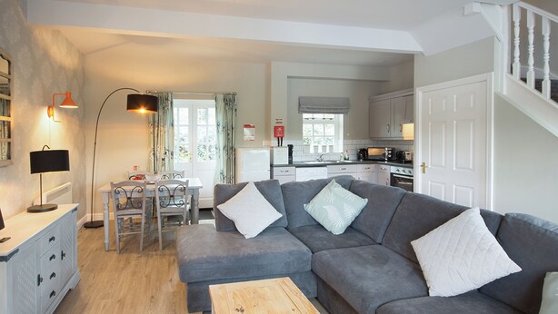 A modern living room with a grey sofa, wooden coffee table, and a dining area with a table and chairs. - Spacious stone cottage set in beautiful woodland with lovely views over a lake. (Darwin Lake, near Matlock)