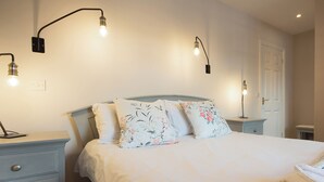 A bedroom with a bed, two bedside tables, and two wall-mounted lamps. - Spacious stone cottage set in beautiful woodland with lovely views over a lake. (Darwin Lake, near Matlock)