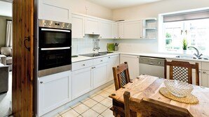 A modern kitchen with white cabinetry, a built-in oven, a dining table with chairs, and a window providing natural light.