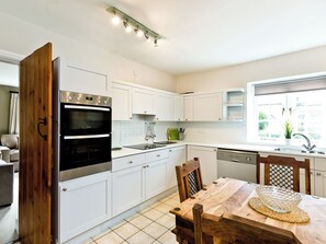 A modern kitchen with white cabinetry, a built-in oven, a dining table with chairs, and a window providing natural light.