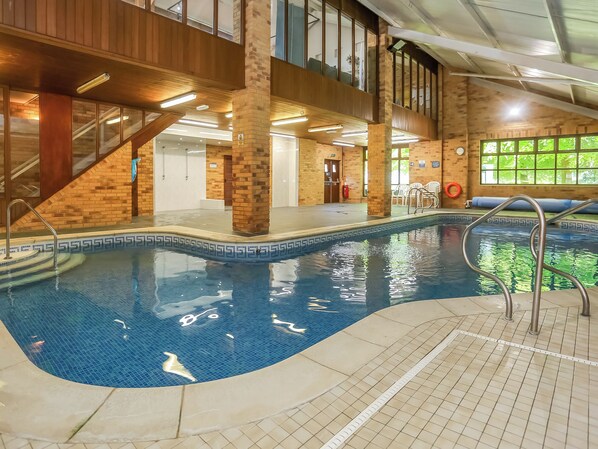 Una piscina interior con borde de azulejos, barandilla metálica y pared de ladrillo.