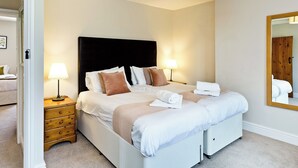 A neatly made bed with pillows, a bedside lamp, a wooden nightstand, and a mirror on the wall.