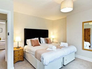 Una cama bien hecha con almohadas, una lámpara de noche, una mesita de madera y un espejo en la pared.