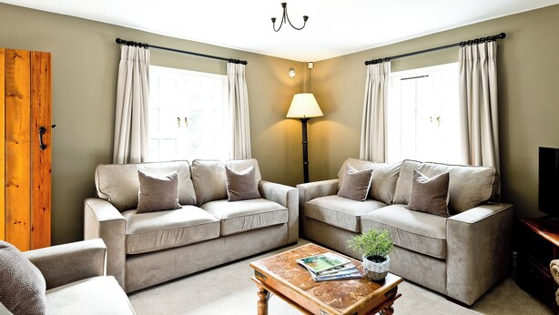 A living room with two sofas, a coffee table, a lamp, and a wooden door. - 5 bedroom accommodation in Carsington, near Ashbourne (Carsington, near Ashbourne)