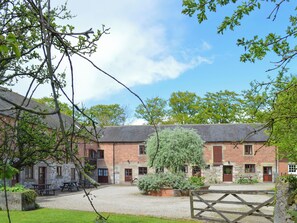 A brick building with multiple windows and doors, a gravel courtyard, and a wooden gate.