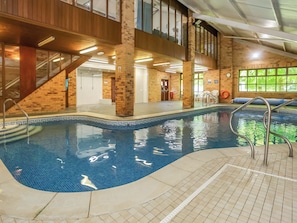An indoor swimming pool with a tiled edge, a metal handrail, and a brick wall.
