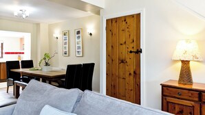 A living room with a sofa, a dining table with chairs, a wooden door, and a lamp. - Attractive barn conversion set in three acres of shared grounds. (Carsington, near Ashbourne)