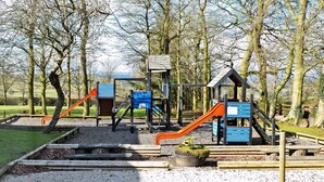 A playground with slides and climbing structures, surrounded by trees and gravel paths. - Attractive barn conversion set in three acres of shared grounds. (Carsington, near Ashbourne)