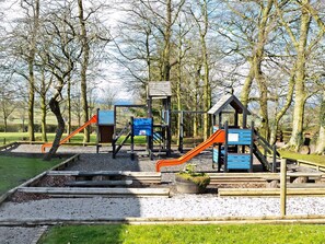 A playground with slides and climbing structures, surrounded by trees and gravel paths. - Attractive barn conversion set in three acres of shared grounds. (Carsington, near Ashbourne)