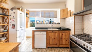 A kitchen with a dishwasher, wooden cabinets, a stove, and a window with a view. - L'Orangerie - Terrasse avec vue sur la montagne (Ajaccio)