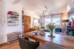 Ein modernes Wohnzimmer mit einem Holzes Esstisch, einer Couch und Blick auf die Stadt.