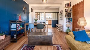 A living room with a sofa, coffee table, bookshelf, and a dining area with chairs and a table. - L'Orangerie - Terrasse avec vue sur la montagne (Ajaccio)