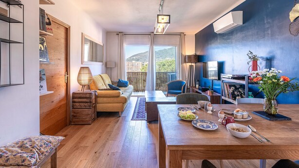 A modern living room with a sofa, dining table, and a view of the outdoors. - L'Orangerie - Terrasse avec vue sur la montagne (Ajaccio)