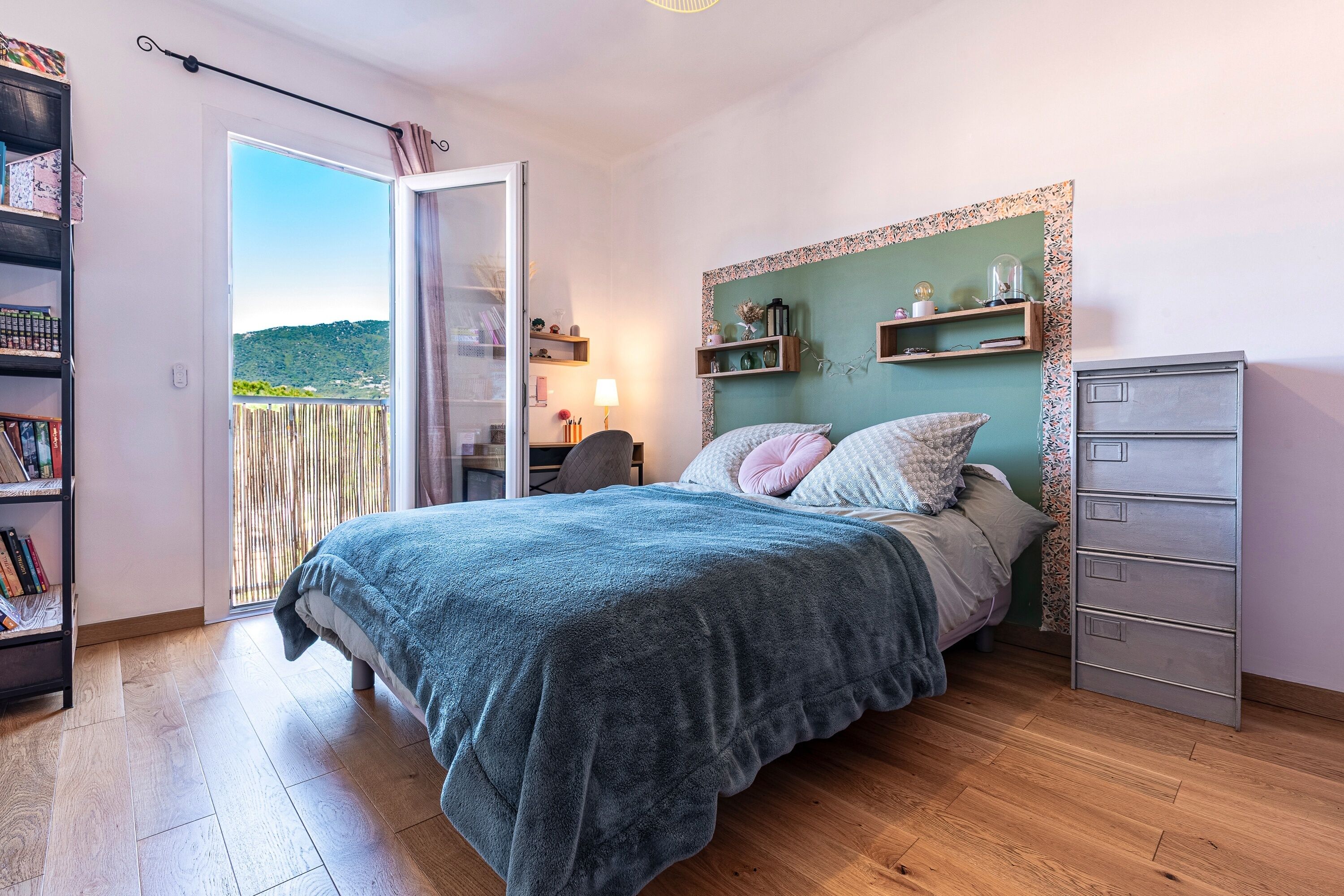 Een slaapkamer met een bed, een kledingkast, een bureau en uitzicht op het omliggende landschap.