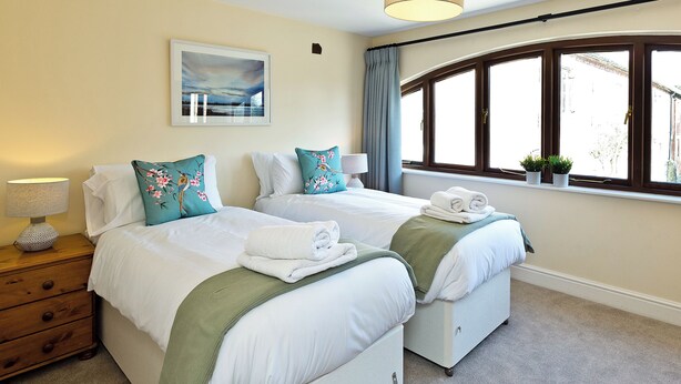 A hotel room with two beds, a window with curtains, a painting on the wall, and a lamp on a nightstand. - 3 bedroom accommodation in Carsington, near Ashbourne (Carsington, near Ashbourne)