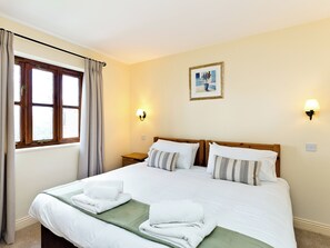 Ett hotellrum med en stor säng, två sängbord, ett fönster med gardiner, en vägglampa och en inramad tavla.