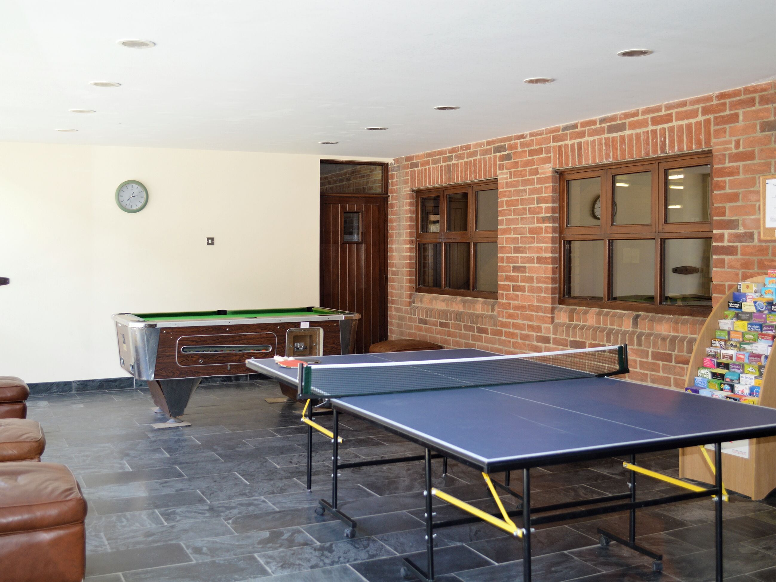 Ein Billardtisch, ein Tischtennis-Tisch und ein Snookertisch in einem Raum mit Backsteinwänden und einer Wanduhr.