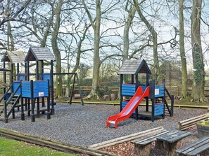 Ein Spielplatz mit Holzspielgeräten, darunter Rutschen und Kletterbereiche, umgeben von Bäumen.