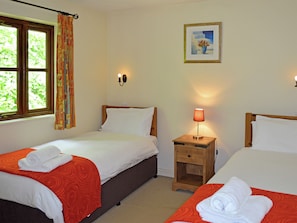 A hotel room with two beds, a nightstand with a lamp, a painting on the wall, and a window with curtains.