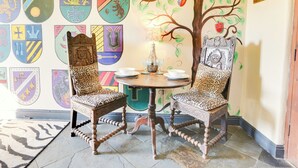 A dining area with two ornate chairs, a table with a vase, and a wall decorated with heraldic shields.