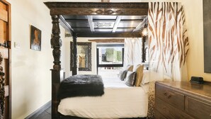 A bedroom with a four-poster bed, a wooden dresser, and a zebra-patterned curtain.