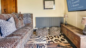 A living room with a sofa, leopard print cushions, a radiator, a framed picture, and a sign for Derbyshire Country Houses.