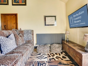 En stue med sofa, leopardmønstrede puder, en radiator, et indrammet billede og et skilt med teksten Derbyshire Country Houses.