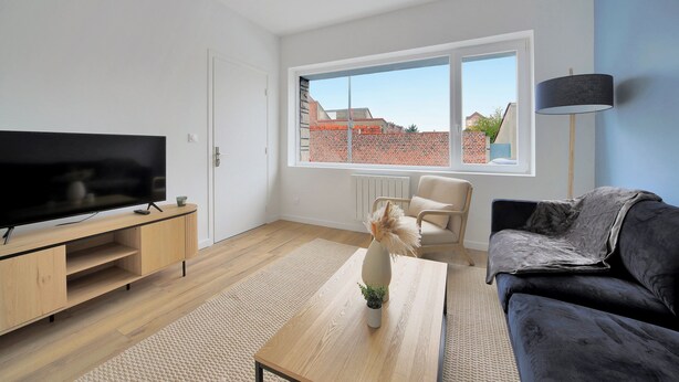 Ein modernes Wohnzimmer mit einem Flachbildfernseher, einem Holztisch, einer Couch und einem großen Fenster mit Blick auf Gebäude.