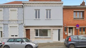 Ein zweistöckiges Gebäude mit weißer Fassade und einem roten Backsteinbereich. Ein Verbotsschild für Fahrzeuge ist auf der rechten Seite sichtbar.