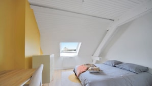 Ein Schlafzimmer mit einem Bett, einem Schreibtisch, einem Stuhl und einem Oberlicht.