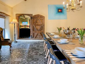 Ein Essbereich mit einem langen Tisch, gedeckt für eine Mahlzeit, einer Kandelaber und einer Holztür.