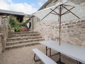 A stone building with a staircase leading to a door, a picnic table, and an umbrella.
