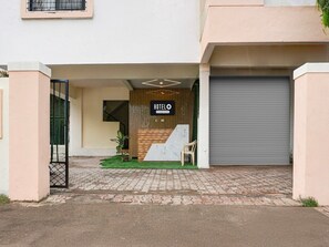 A hotel entrance with a wooden reception desk, a signboard, a potted plant, and a closed garage door. - Hotel O Laxman Nagar Baner (Pune)