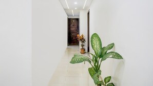 A hallway with white walls, a potted plant, and a door at the end. - Hotel O Laxman Nagar Baner (Pune)