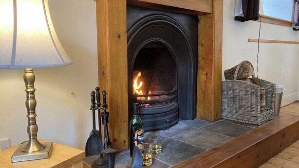 Een haard met gloeiende blokken hout, een lamp, een fles Glenfarclas whisky en een rieten mand.