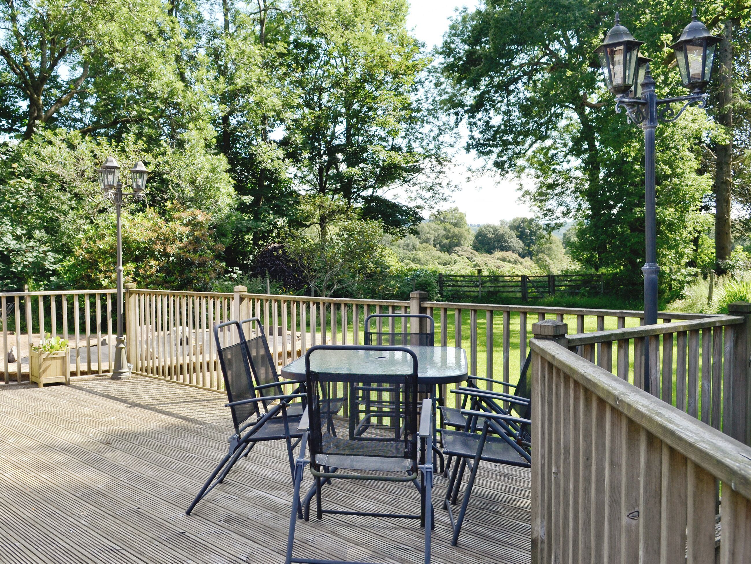 An outdoor patio with a table and chairs, surrounded by a wooden deck and a fence.