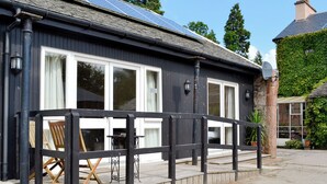 Een huis met een donkere gevel, grote ramen, een houten terras en zonnepanelen op het dak.