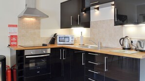 Een moderne keuken met zwarte kastjes, een magnetron, een waterkoker en een brandblusser.