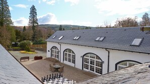 Une maison dotée d’une cour avec un échiquier, d’un toit en pierre et offrant une vue sur le paysage environnant.