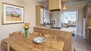 Une cuisine avec des meubles de rangement en bois, une table à manger avec des chaises, un vase de fleurs et un tableau accroché au mur.