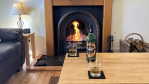 Een gezellige woonkamer met een open haard, een houten tafel met een fles en een glas, en een donker leren bank.