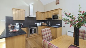 Cocina moderna con armarios de madera, encimera negra, microondas y comedor con sillas a cuadros.