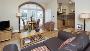 Een moderne woonkamer met een bank, salontafel, televisie en een eethoek met stoelen en een kroonluchter.