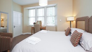 Een hotelkamer met een bed, een bureau, een stoel, een lamp en een raam met jaloezieën.